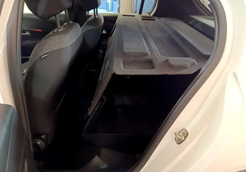 Vue côté droit arrière d'une Peugeot 208 électrique blanche avec banquette arrière rabattue et coffre ouvert.