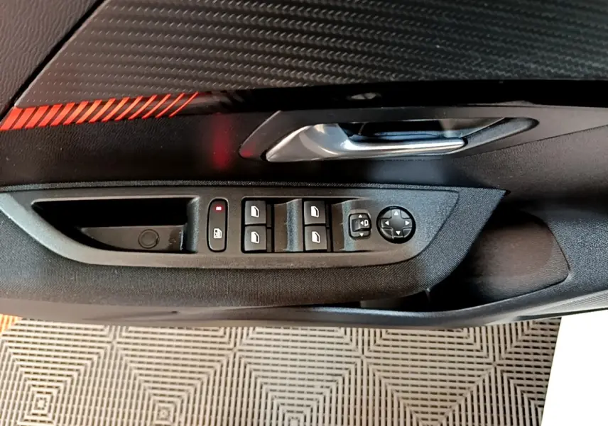 Vue rapprochée de la portière côté conducteur du Peugeot 208 électrique blanc, avec commandes des vitres et rétroviseurs.