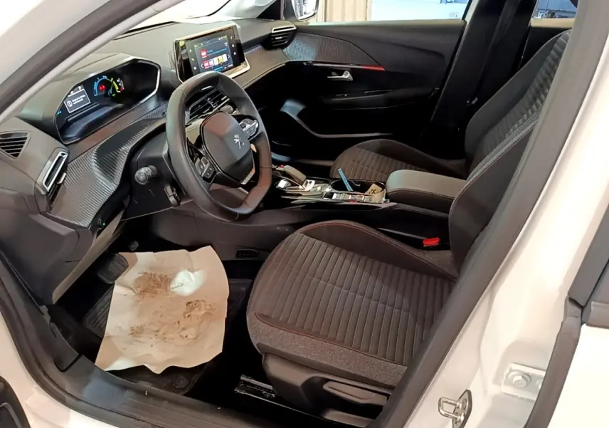 Intérieur avant droit d'une Peugeot 208 électrique blanche 2022, tableau de bord avec écran tactile et sièges tissu noirs.