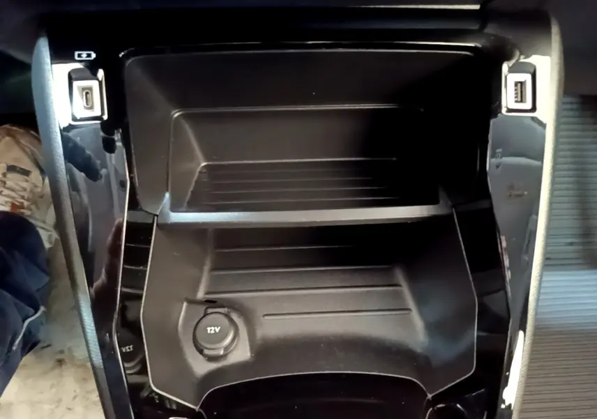 Vue rapprochée de la console centrale noire avec prises USB et prise 12V du Peugeot 208 électrique blanc.