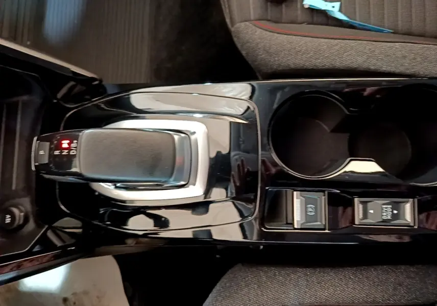 Vue plongeante sur la console centrale noire de la Peugeot 208 électrique avec levier de vitesse automatique et porte-gobelets.