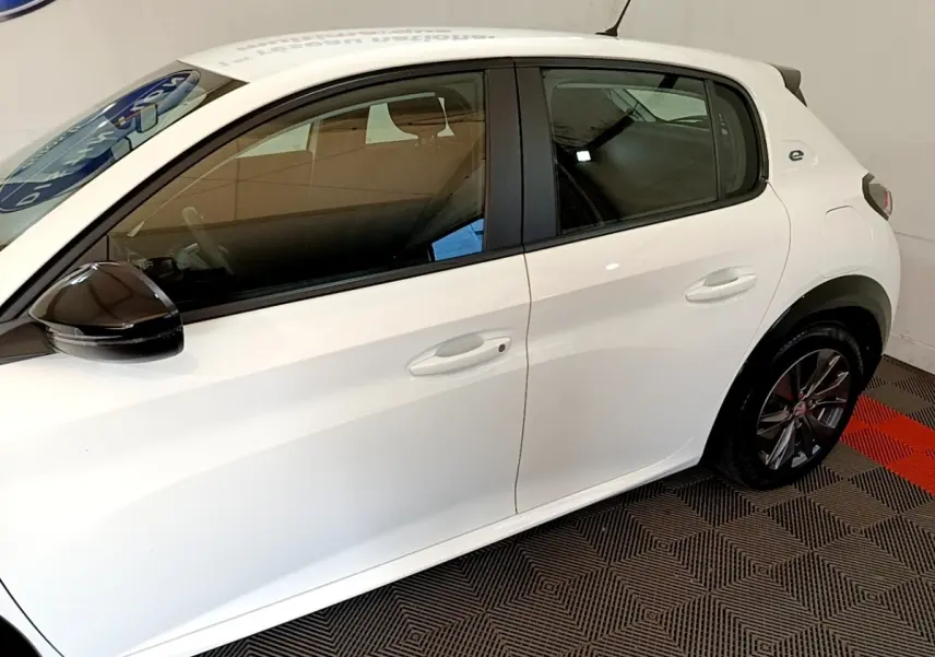 Profil côté gauche d'une Peugeot 208 électrique blanche avec rétroviseur noir et jantes alliage foncé.