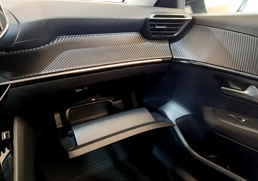 Intérieur de la Peugeot 208 électrique 2022, vue côté passager avec boîte à gants ouverte et finition carbone.