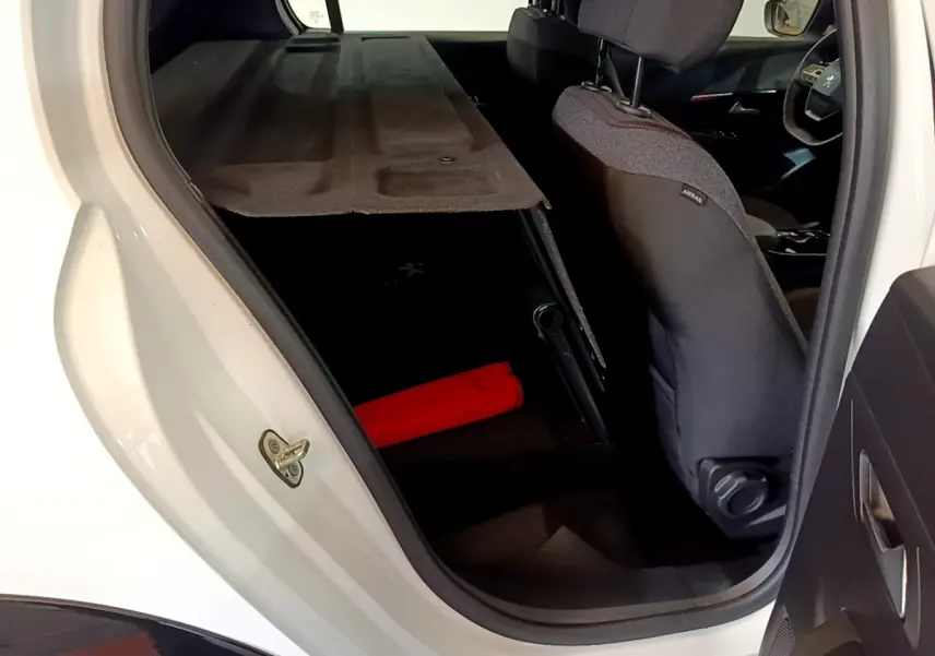 Vue intérieure côté arrière droit du coffre ouvert d'une Peugeot 208 électrique blanche avec cache-bagages déployé.