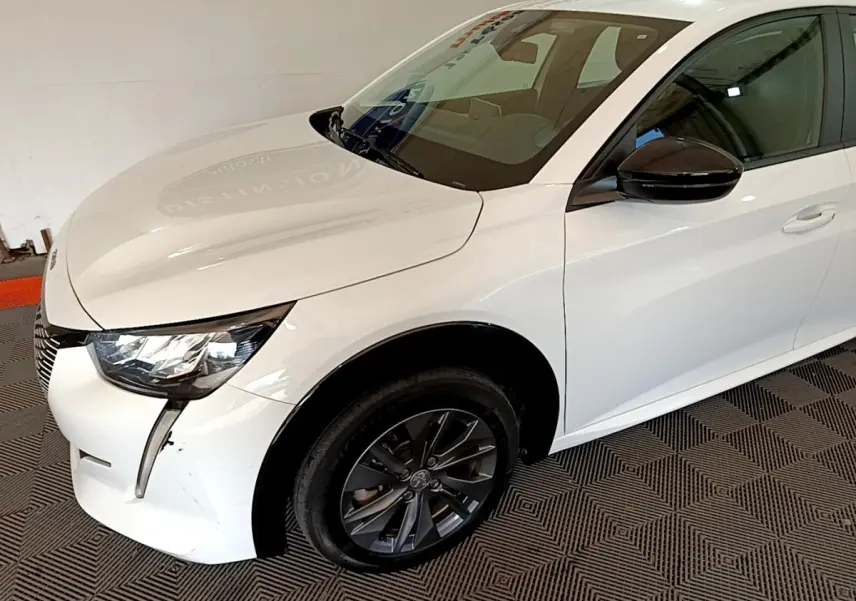 Vue 3/4 avant droit d'une Peugeot 208 électrique blanche avec rétroviseur noir et jante foncée.