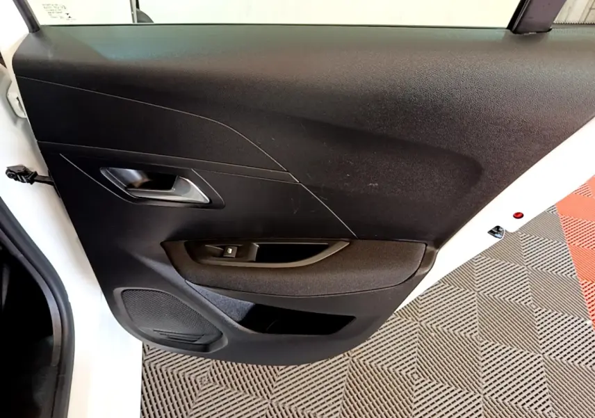 Vue rapprochée de la porte arrière gauche noire d’une Peugeot 208 électrique blanche, avec poignée et commande de vitre.