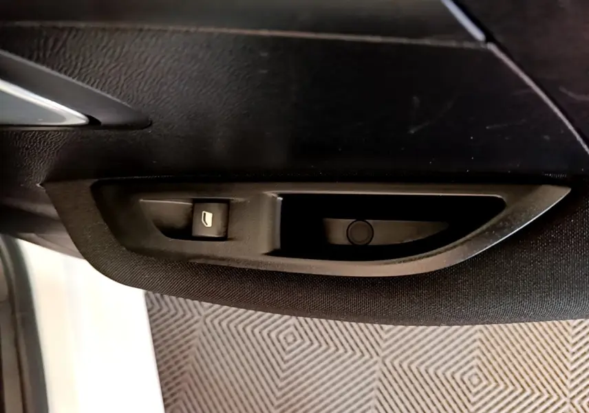 Gros plan sur la commande de lève-vitre électrique côté conducteur de la Peugeot 208 électrique blanche, intérieur noir.