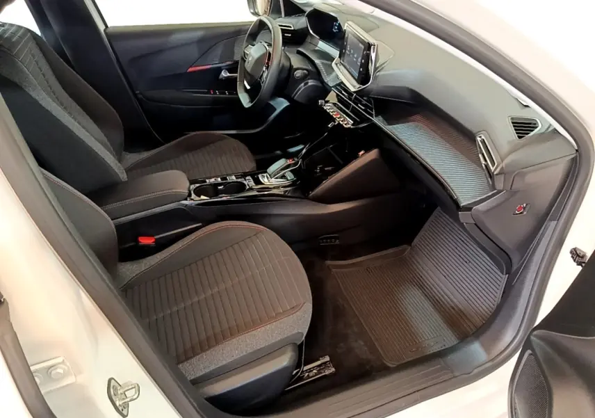 Vue intérieure côté passager de la Peugeot 208 électrique blanche, avec tableau de bord moderne et sièges noirs.