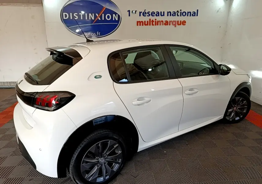 Peugeot 208 électrique blanche vue 3/4 arrière droit, avec jantes foncées et logo "e" vert sur l'aile arrière.