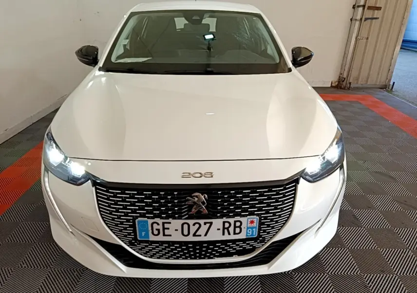 Vue avant d'une Peugeot 208 électrique blanche avec phares allumés et calandre noire distinctive.