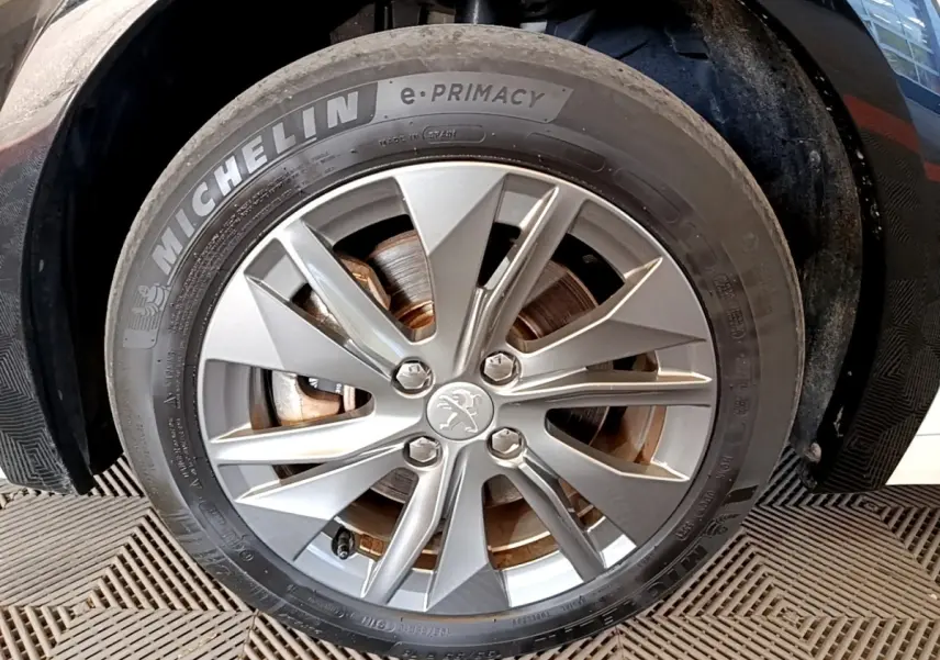 Gros plan sur la roue avant gauche d’une Peugeot 208 électrique blanche, jante alliage avec logo lion au centre.