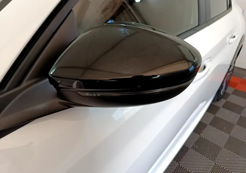 Rétroviseur noir côté gauche en gros plan sur Peugeot 208 électrique blanche vue partielle côté conducteur.