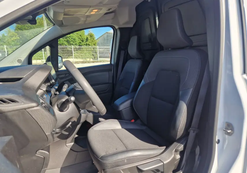 Vue intérieure côté conducteur du Renault Kangoo blanc 2023, mettant en valeur les sièges noirs et le tableau de bord simple.