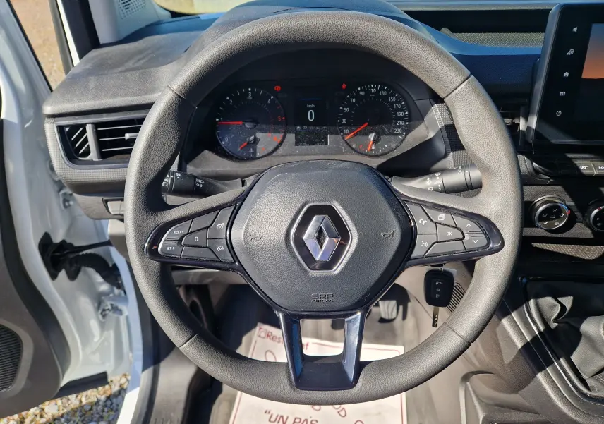 Vue rapprochée du volant noir du Renault Kangoo blanc 2023, avec commandes intégrées et tableau de bord visible.