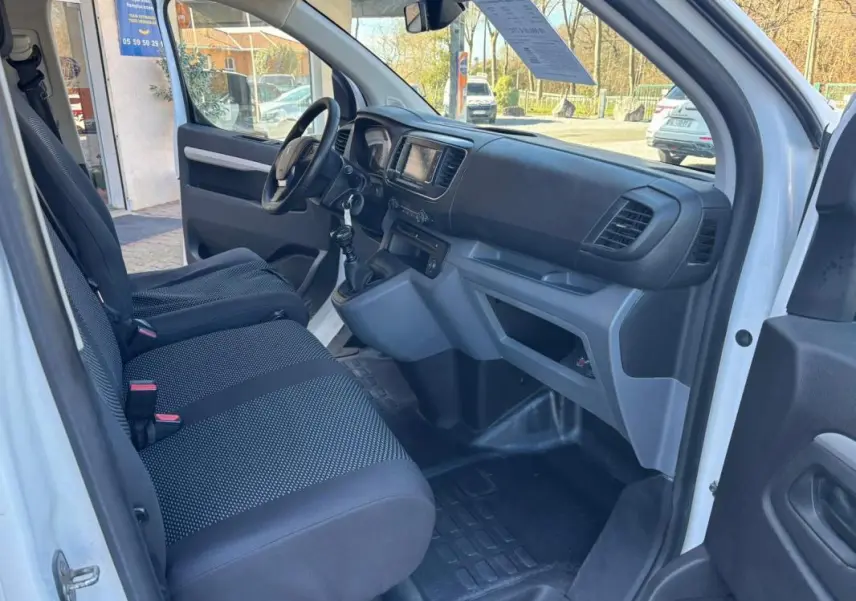 Vue intérieure côté conducteur du Peugeot Expert Fourgon blanc de 2018, montrant le tableau de bord et les sièges noirs.