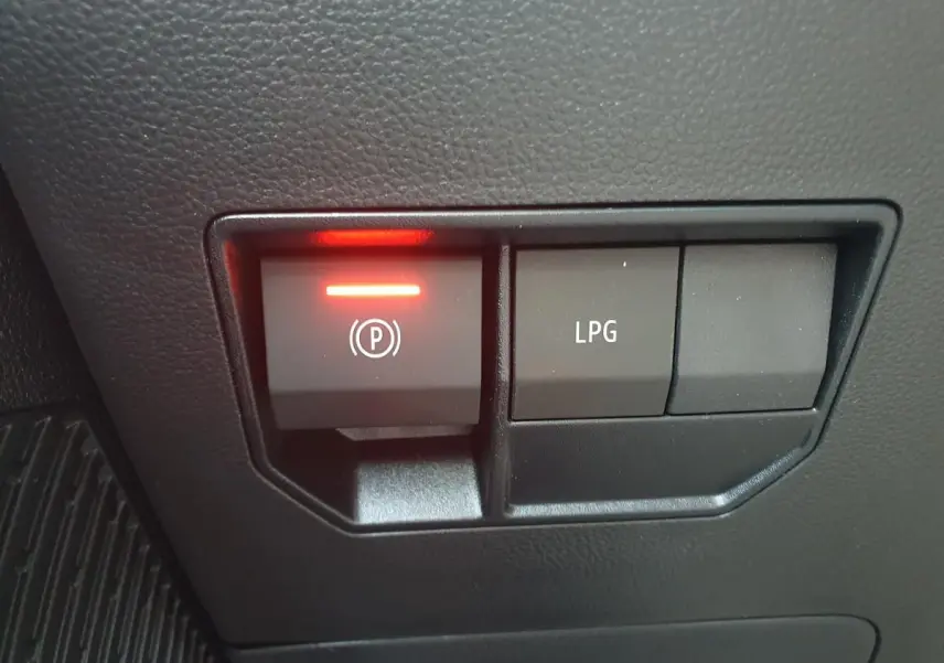 Gros plan sur les boutons de commande du frein de stationnement et du mode GPL dans l'habitacle du Dacia Duster gris schiste.