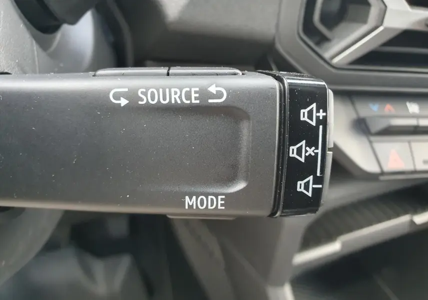Gros plan sur la commande au volant du Dacia Duster 2026 gris schiste, avec boutons source et mode visibles.
