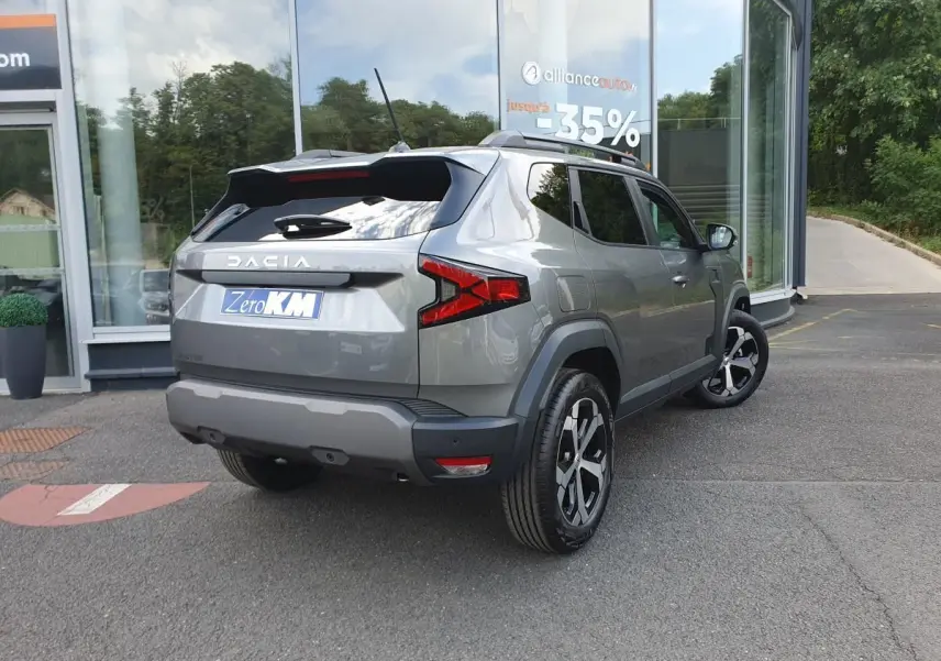 Vue 3/4 arrière droite du Dacia Duster gris schiste métallisé avec jantes alliage et barres de toit fixes.