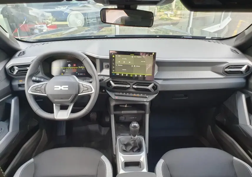 Vue intérieure frontale du tableau de bord du Dacia Duster 2026 avec écran tactile central et volant multifonction noir.