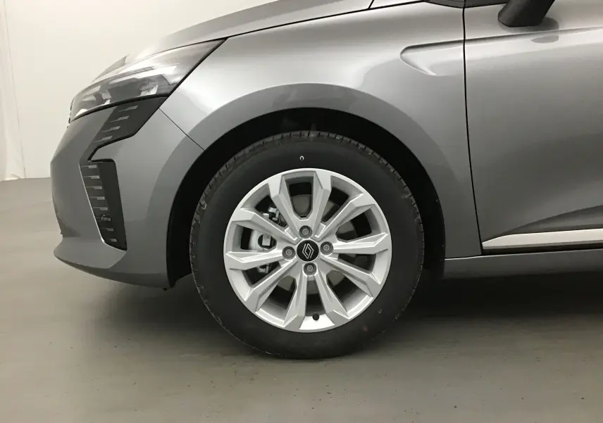 Gros plan sur la roue avant gauche d'une Renault Clio V gris schiste, avec jante alliage et partie avant du véhicule visible.