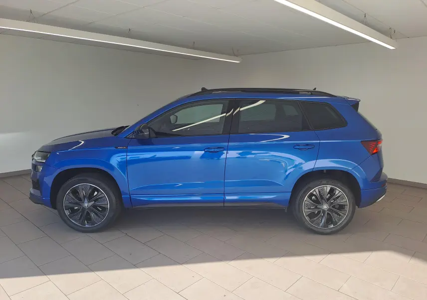 Profil côté gauche d'un Skoda Karoq 2025 bleu RS avec toit panoramique ouvrant et jantes alliage distinctives.