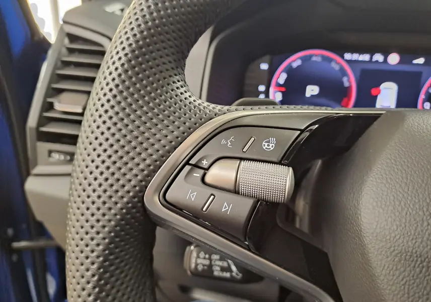Gros plan sur les commandes gauche du volant perforé d’un Skoda Karoq Bleu RS 2025 avec tableau de bord numérique en arrière-plan.