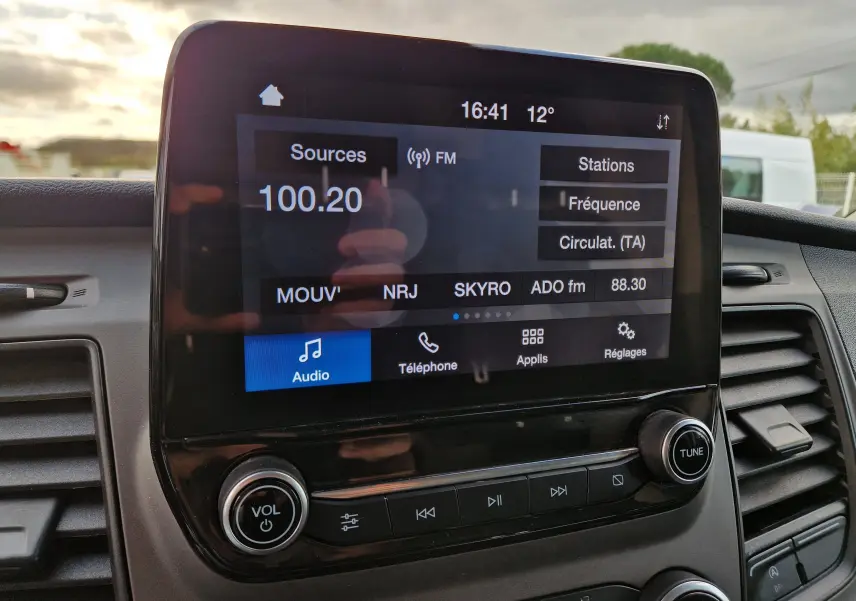 Vue rapprochée de l’écran tactile multimédia du Ford Transit Custom blanc, affichant la radio FM à 100.20 MHz.