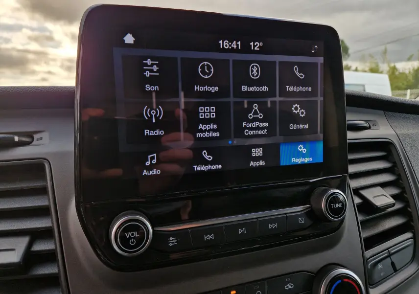 Écran tactile central du Ford Transit Custom blanc, affichant le menu principal avec options son, Bluetooth et réglages.
