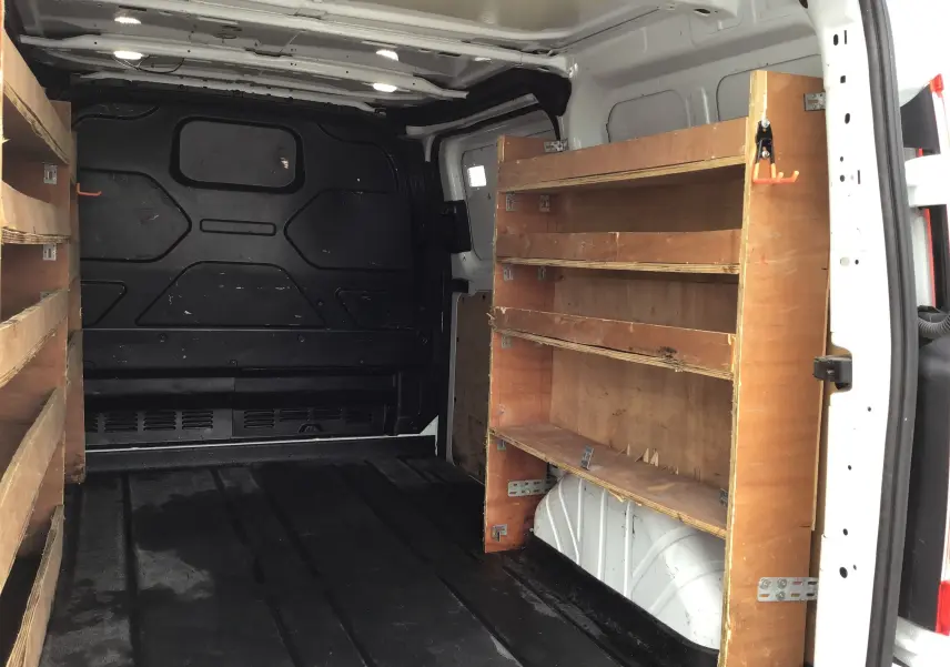 Vue intérieure arrière droite d’un Ford Transit Custom blanc 2021 avec étagères en bois intégrées dans le fourgon.