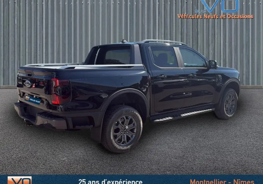 Ford Ranger Wildtrak noir en 3/4 arrière droit, avec barres de toit, marchepieds et jantes alliage 18 pouces.