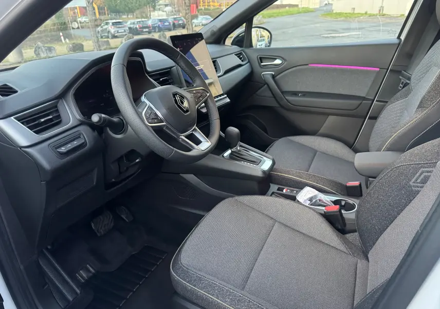 Vue intérieure côté conducteur du Renault Captur E-Tech hybride 2025, sièges gris et tableau de bord noir avec écran tactile vertical.