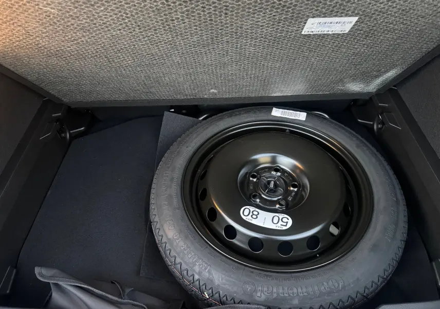 Roue de secours noire dans le coffre d’un Renault Captur blanc nacré toit noir, vue en plongée sur le pneu.
