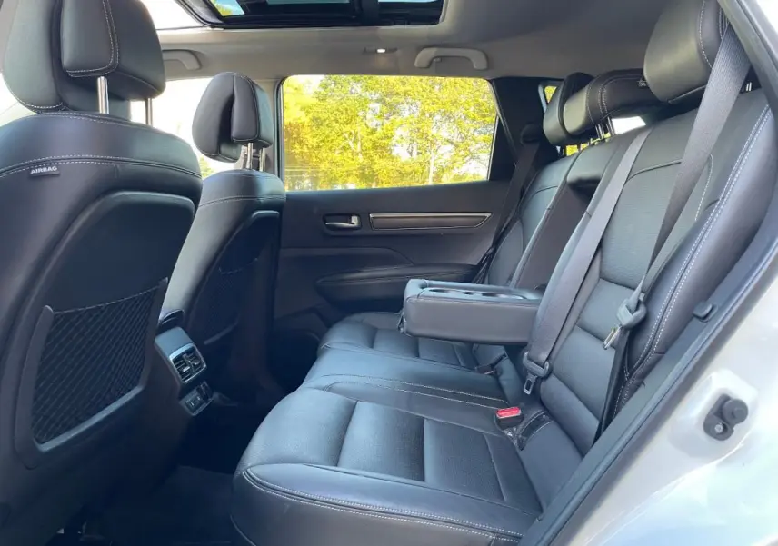 Vue intérieure côté droit du Renault Koleos blanc 2019, montrant les sièges arrière en cuir avec accoudoir central et toit ouvrant panoramique.
