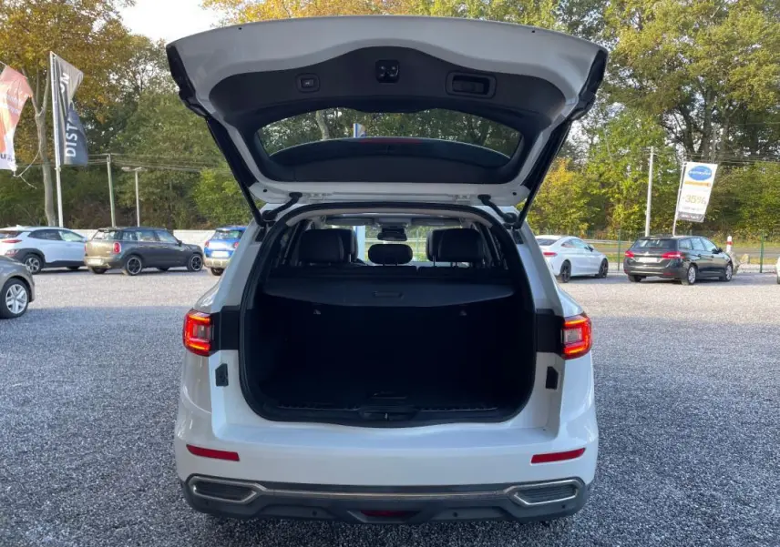 Vue arrière d'un Renault Koleos blanc 2019 avec coffre ouvert, montrant l'espace de chargement et les feux arrière allumés.