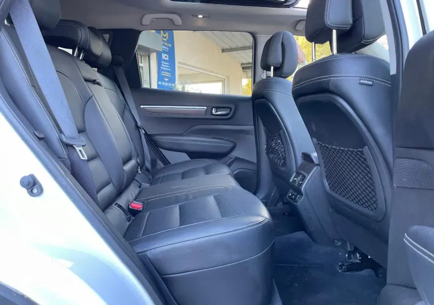 Vue intérieure côté arrière gauche du Renault Koleos blanc 2019, montrant les sièges en cuir noir et le toit ouvrant panoramique.