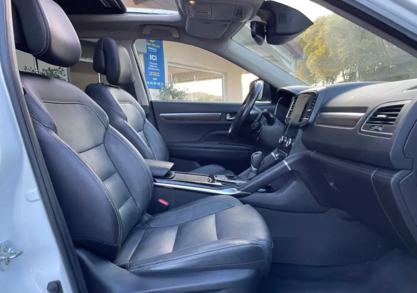 Vue intérieure côté gauche du Renault Koleos blanc 2019, sièges cuir noirs et toit ouvrant panoramique visibles.