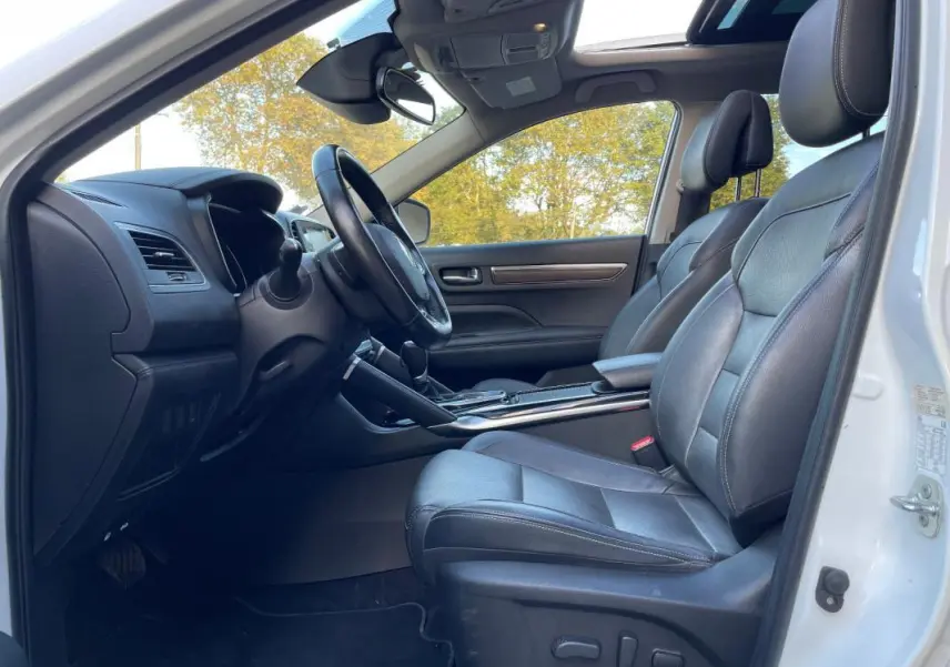 Vue intérieure côté conducteur du Renault Koleos blanc 2019 avec sièges cuir noirs et toit ouvrant panoramique visible.