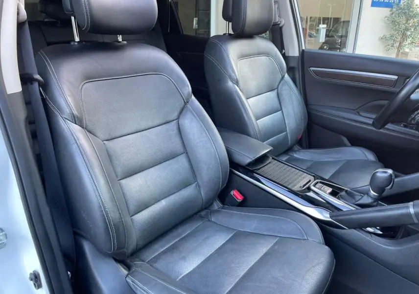 Vue intérieure des sièges avant en cuir noir du Renault Koleos blanc 2019, avec accoudoir central et console centrale visible.