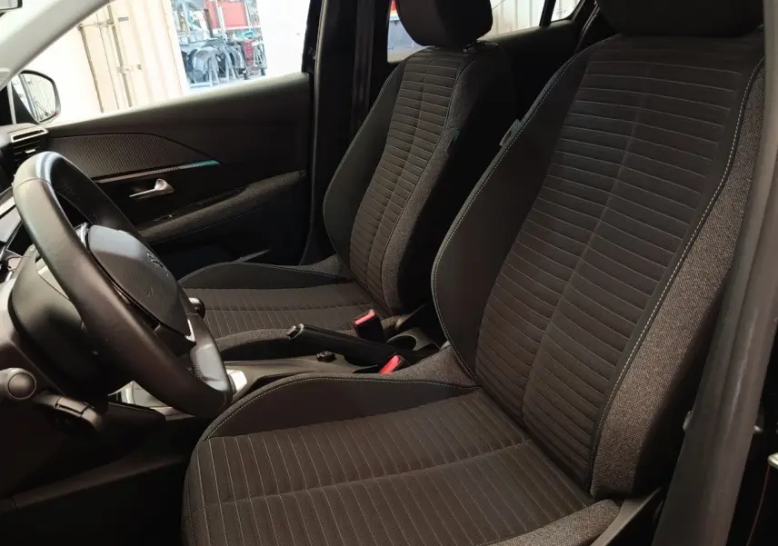 Vue intérieure côté conducteur de la Peugeot 208 PureTech 100 S&S Style 2022 avec sièges tissu noirs et volant cuir multifonctions.
