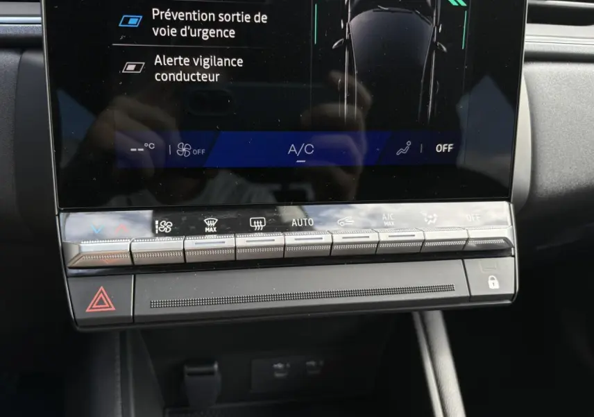 Détail du tableau de bord noir du Renault Symbioz 2025 avec commandes climatisation et écran tactile affichant alertes de sécurité.
