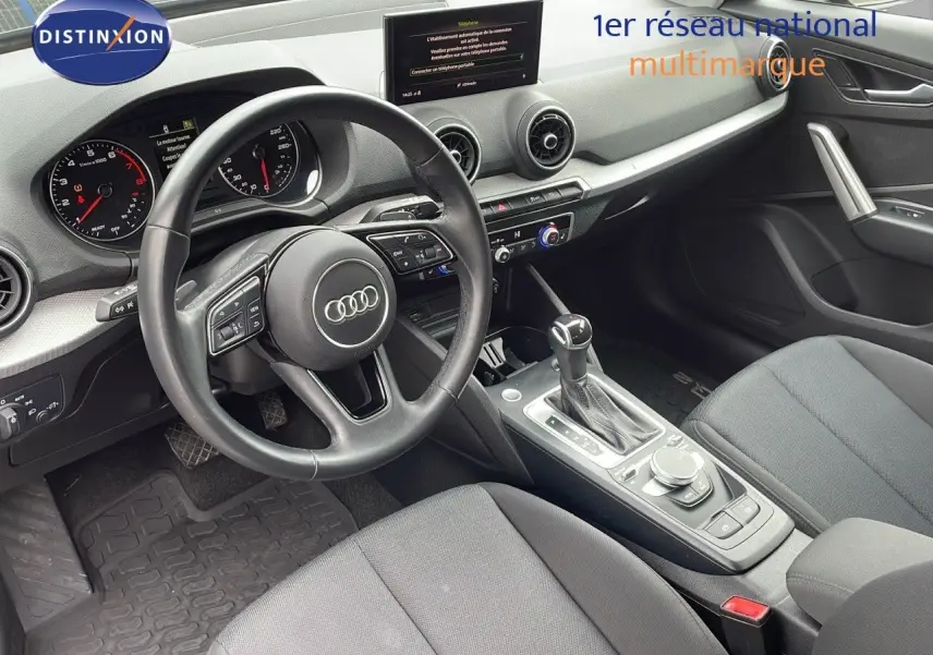 Vue intérieure de l'Audi Q2 35 TFSI 2023, montrant le poste de conduite avec volant, tableau de bord et console centrale en tissu gris.