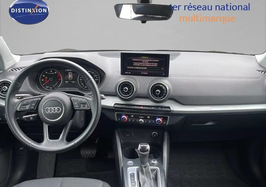 Vue intérieure de l'Audi Q2 2023 S-Line, tableau de bord et volant noir avec écran central et commandes climatisation visibles.