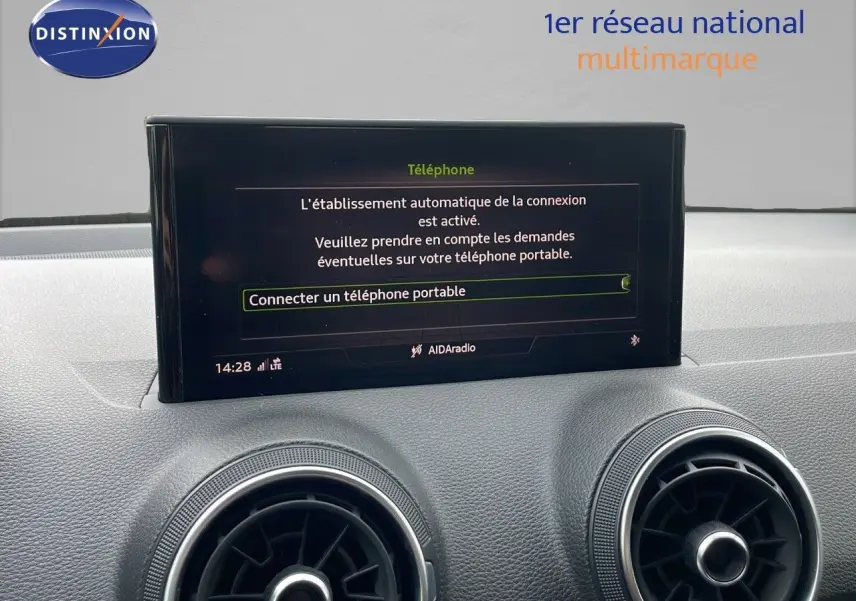 Vue intérieure du tableau de bord de l'Audi Q2 2023, écran central affichant la connexion téléphone, entouré de sorties d'air rondes.