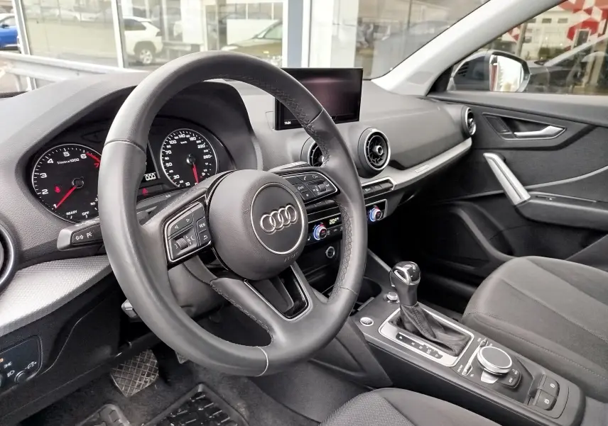 Intérieur de l'Audi Q2 35 TFSI 2023 vu côté conducteur, avec volant cuir, tableau de bord noir et console centrale moderne.