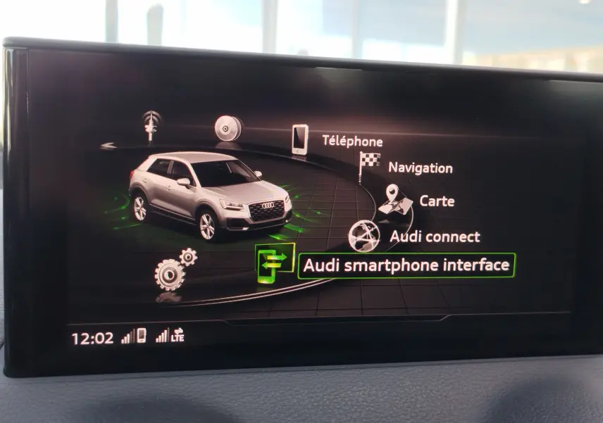 Écran central affichant l'interface multimédia avec une Audi Q2 gris clair vue de trois quarts avant.