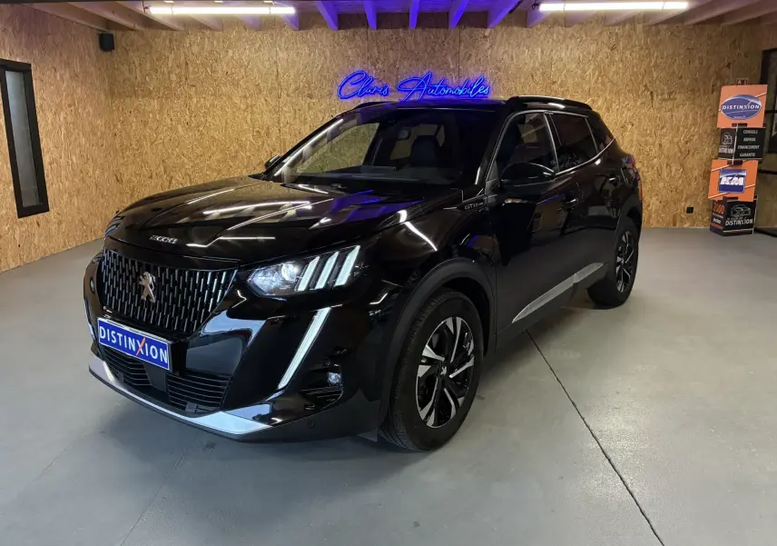 Peugeot 2008 noir 3/4 avant droit en intérieur, avec calandre distinctive et jantes bi-ton visibles.