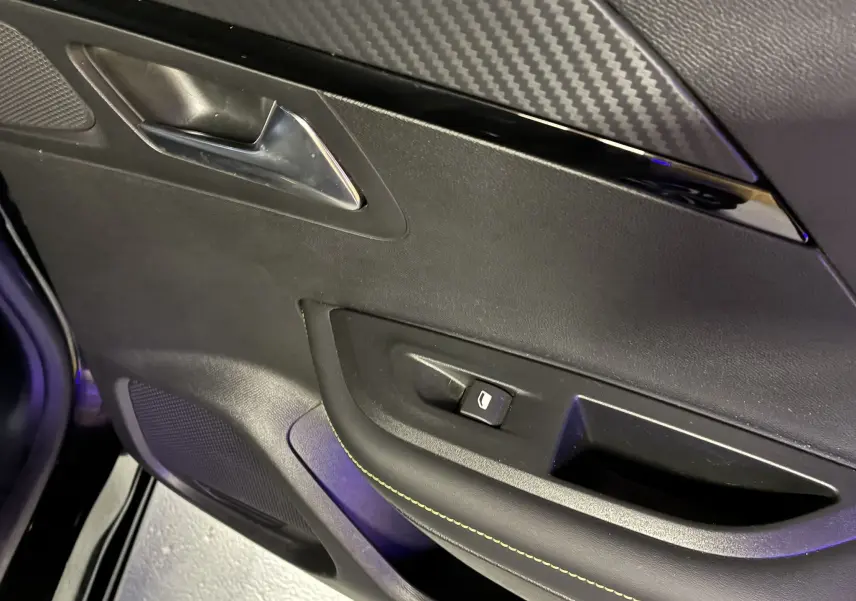 Détail de la porte intérieure côté gauche du Peugeot 2008 noir, avec poignée chromée et bouton de commande de vitre.