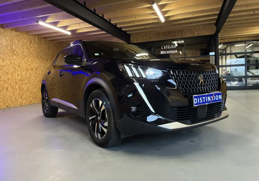 Peugeot 2008 noir vue 3/4 avant droit, avec calandre distinctive et feux LED allumés en intérieur d'atelier.