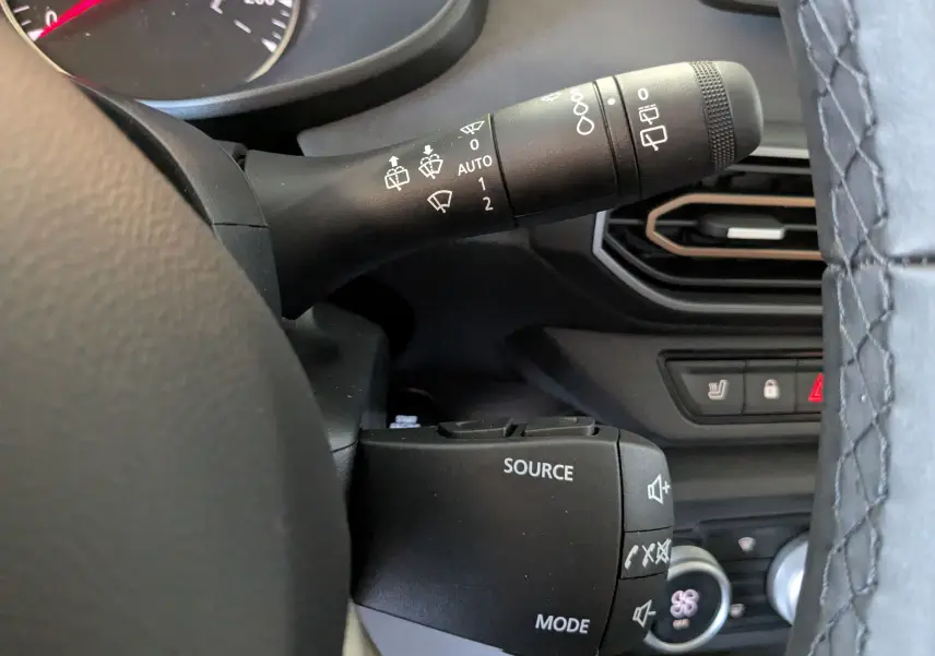 Gros plan sur les commandes au volant et manette d’essuie-glace du tableau de bord intérieur du Dacia Jogger gris schiste.