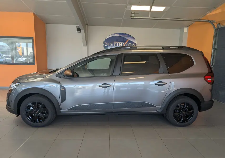 Vue de profil droit du Dacia Jogger gris schiste métal 2026 avec jantes noires et décorations latérales distinctives.